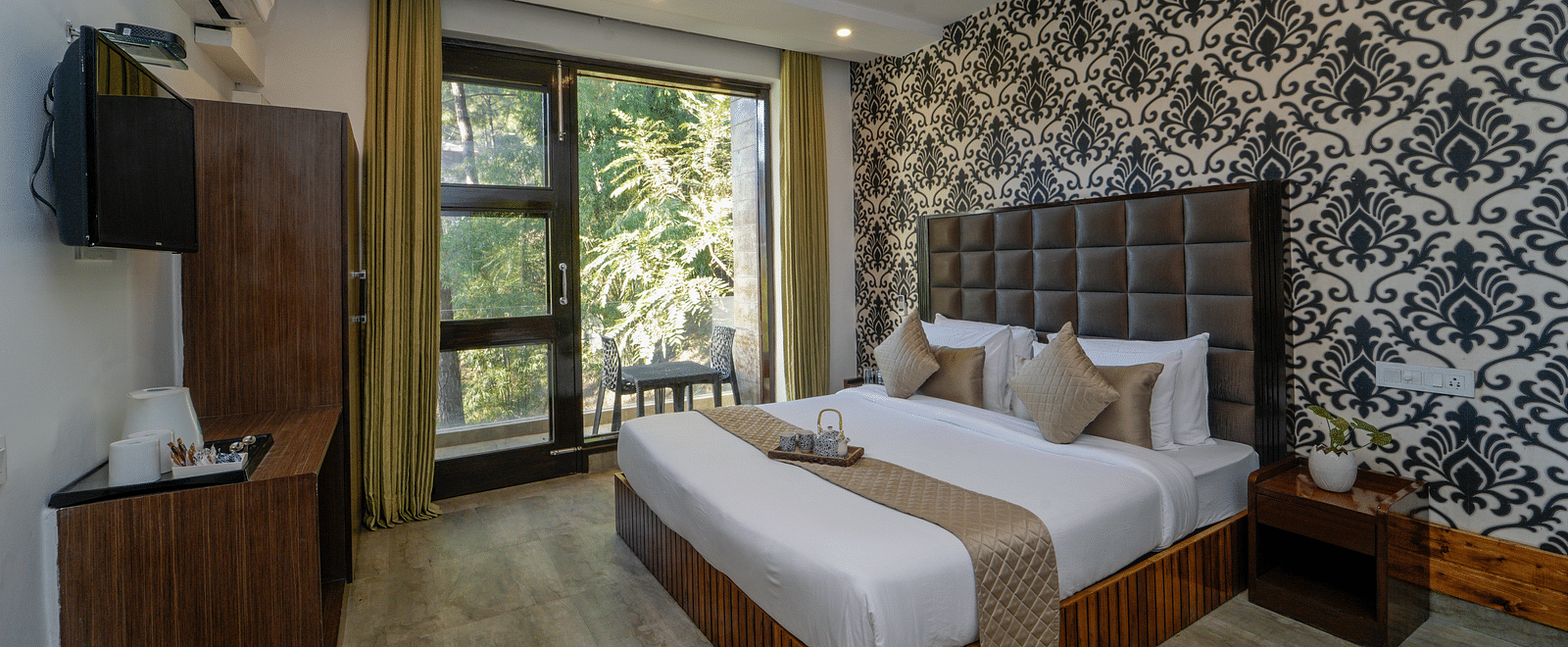 The deluxe room at DLS Whispering Winds featuring a bed, bed side tables, flat screen TV, other room amenities and a glass door leading to the balcony